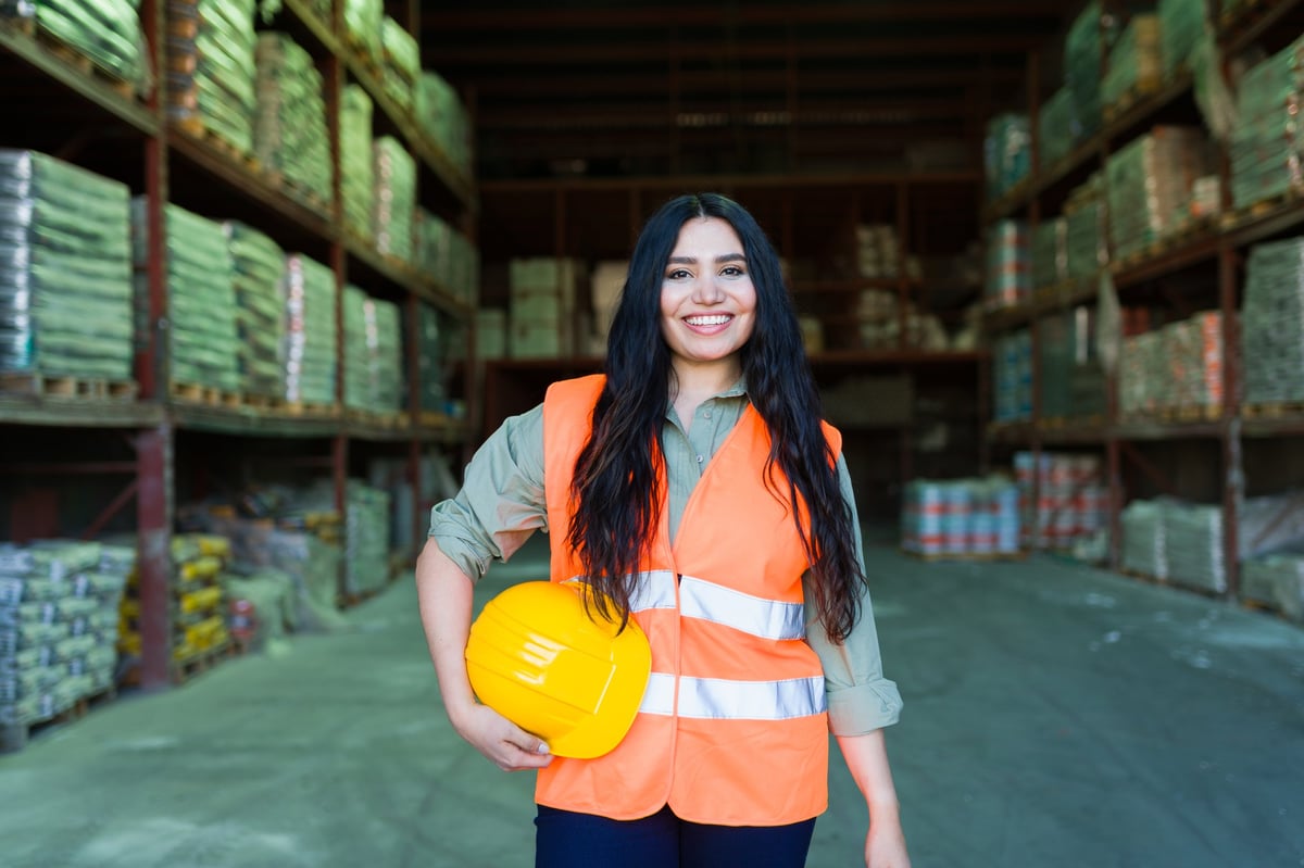 Lachende vrouw in veiligheidsvest voor een industrieel magazijn